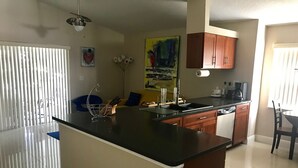 A modern kitchen with a central island, wooden cabinets, and a dining area with a chair. - PERFECT RELAXING  GETAWAY FOR COUPLE OR SMALL GROUP (Boynton Beach)