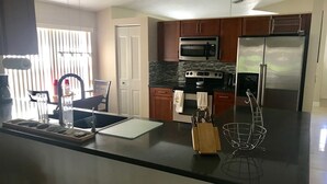 A modern kitchen with a black countertop, stainless steel appliances, and wooden cabinets. - PERFECT RELAXING  GETAWAY FOR COUPLE OR SMALL GROUP (Boynton Beach)