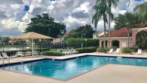 A swimming pool with lounge chairs and umbrellas, surrounded by palm trees and houses. - PERFECT RELAXING  GETAWAY FOR COUPLE OR SMALL GROUP (Boynton Beach)