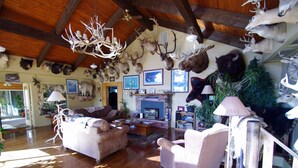 A rustic living room with a fireplace, leather sofas, and a chandelier made of antlers. - Whitebird Summit 7 bedroom home (Grangeville)