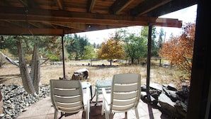 A covered outdoor seating area with two white chairs and a table, overlooking a natural landscape with trees and a fence. - Whitebird Summit 7 bedroom home (Grangeville)