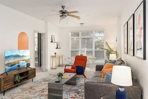Una sala de estar con televisor, sofá, sillón, mesa de centro y ventilador de techo.