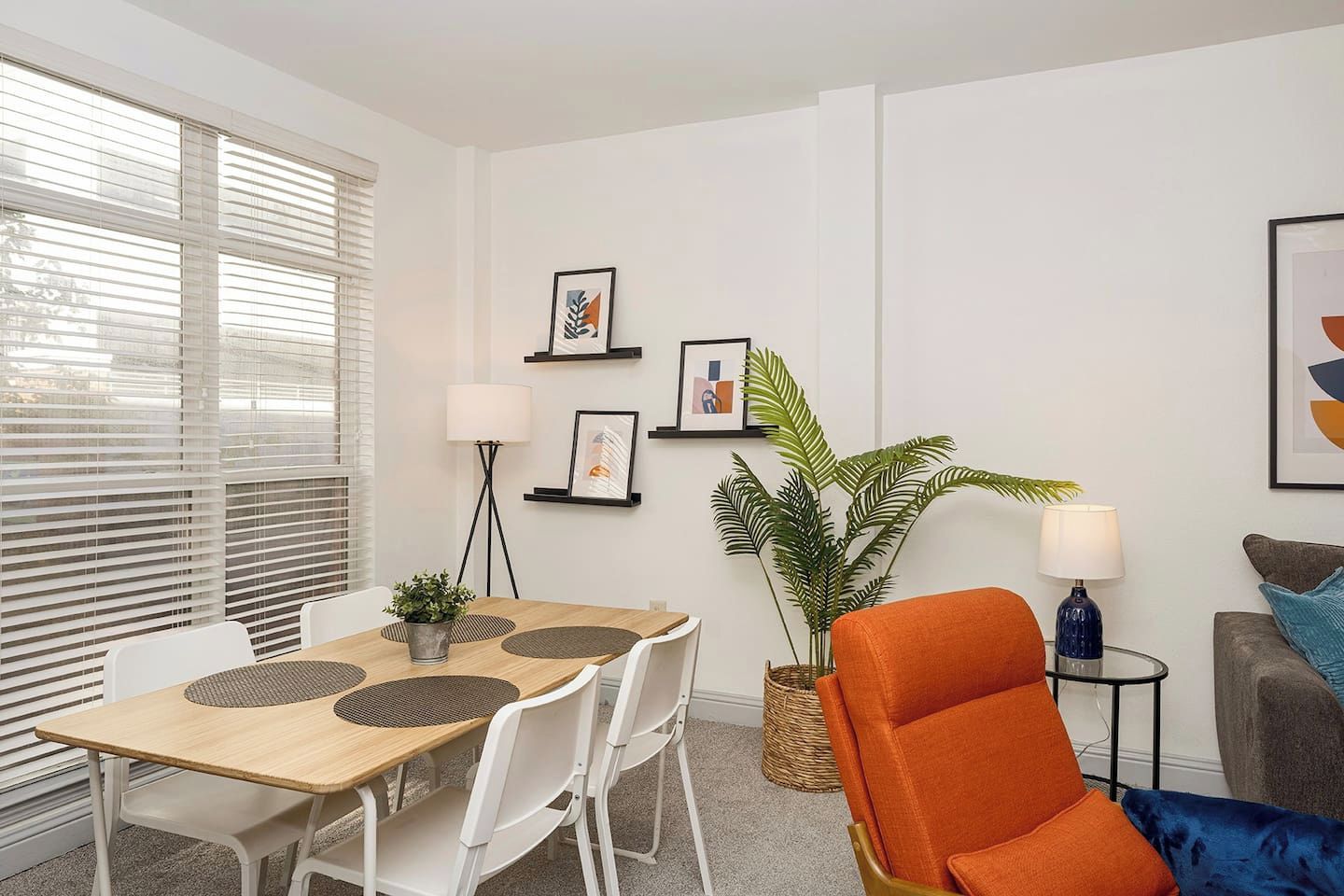 A modern living room with a dining table, white chairs, a large plant, and a sofa with cushions.