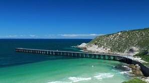 A coastal scene with a long pier extending into the ocean, a sandy beach, and a rocky hill in the background. - Driftaway -WIFI, NETFLIX, pet friendly, Comfort + Undercover deck with hammock (Marion Bay)