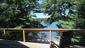 A wooden deck with a metal railing overlooking a lake, surrounded by trees. - Beach Front on Beautiful Jenkins Pond, Quiet Area, 
Discounted off season rates! (East Falmouth)