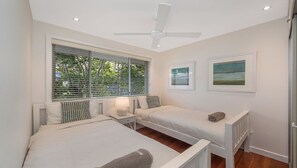 A bedroom with two beds, a ceiling fan, and artwork on the wall. - Footsteps to the Bay by HolidayCo. (Pretty Beach)