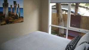 A bedroom with a large window, a painting on the wall, and a bed with pillows.