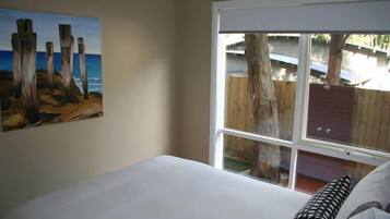 Une chambre avec une grande fenêtre, un tableau au mur et un lit avec des oreillers.