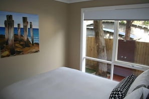 A bedroom with a large window, a painting on the wall, and a bed with pillows. - Lorne Surfdogz at Lorne (Lorne)