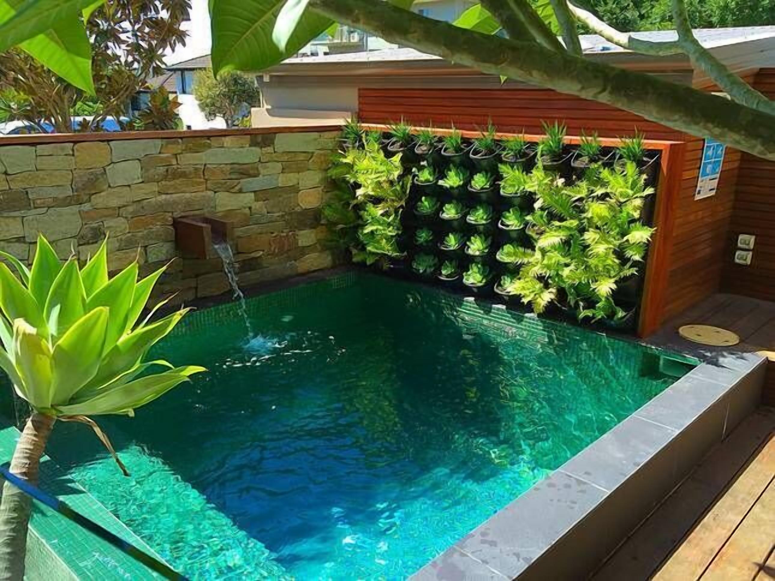 Une piscine avec un mur en pierre et une terrasse en bois.