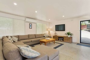 A modern living room with a sectional sofa, a coffee table, a lamp, a TV mounted on the wall, and a sliding glass door leading to an outdoor area. - Portsea Escape (Portsea)