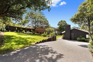 A residential driveway leading to a house with a dark exterior, surrounded by lush greenery and trees. - Portsea Escape (Portsea)