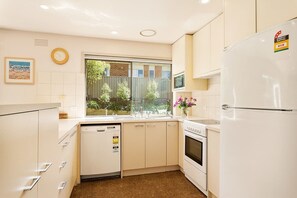 A kitchen with white cabinets, a dishwasher, an oven, and a refrigerator. - Portsea Escape (Portsea)