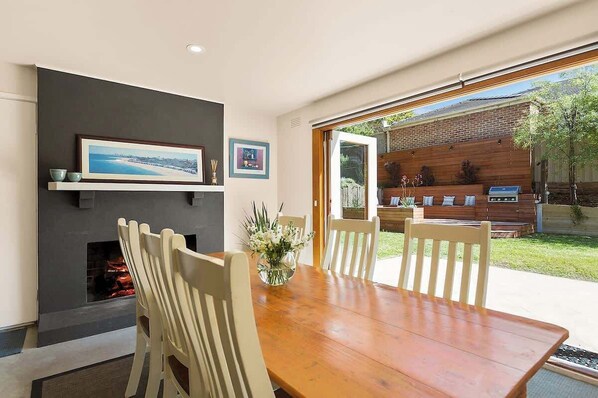 A dining area with a wooden table and chairs, a fireplace, and a view of an outdoor barbecue area.