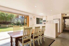 A dining area with a wooden table and chairs, a kitchen with white cabinets, and a view of the outdoors.
