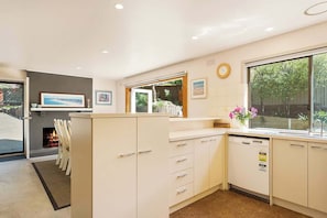 A modern kitchen with white cabinetry, a built-in dishwasher, and a large window offering a view of the outdoors.