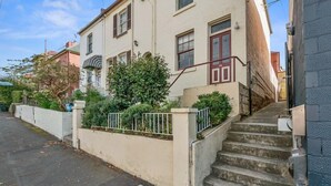 A residential building with a staircase leading to the entrance, a small garden area, and a manhole cover on the pavement.