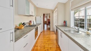 A modern kitchen with white cabinets, a wooden floor, and a large window providing natural light.