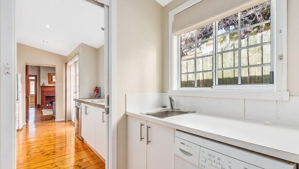 A laundry room with a washing machine, a sink, and a window with a view of trees.