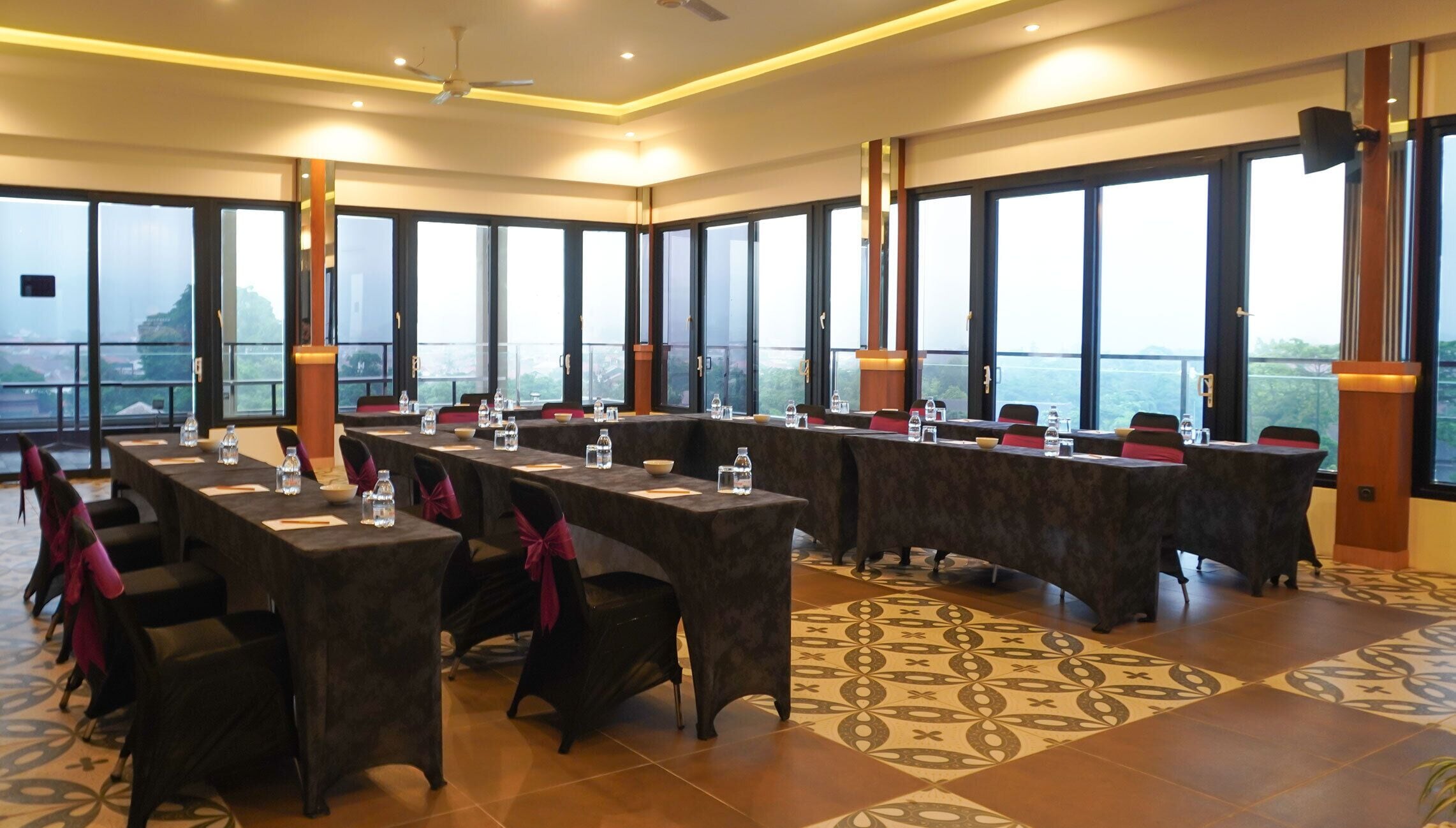 A conference room with long tables, chairs, and large windows offering a view of the outdoors.