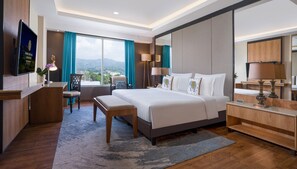 A modern hotel room with a large bed, a desk, a chair, a TV, and a view of the mountains. - Grand Sunshine Resort & Convention (Soreang)
