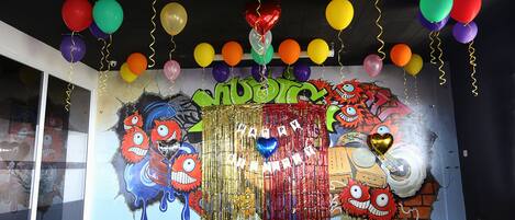 A room with a colorful balloon arrangement and a birthday-themed mural on the wall.