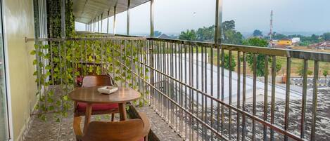A balcony with a table and chairs, a view of a road, and a metal railing.