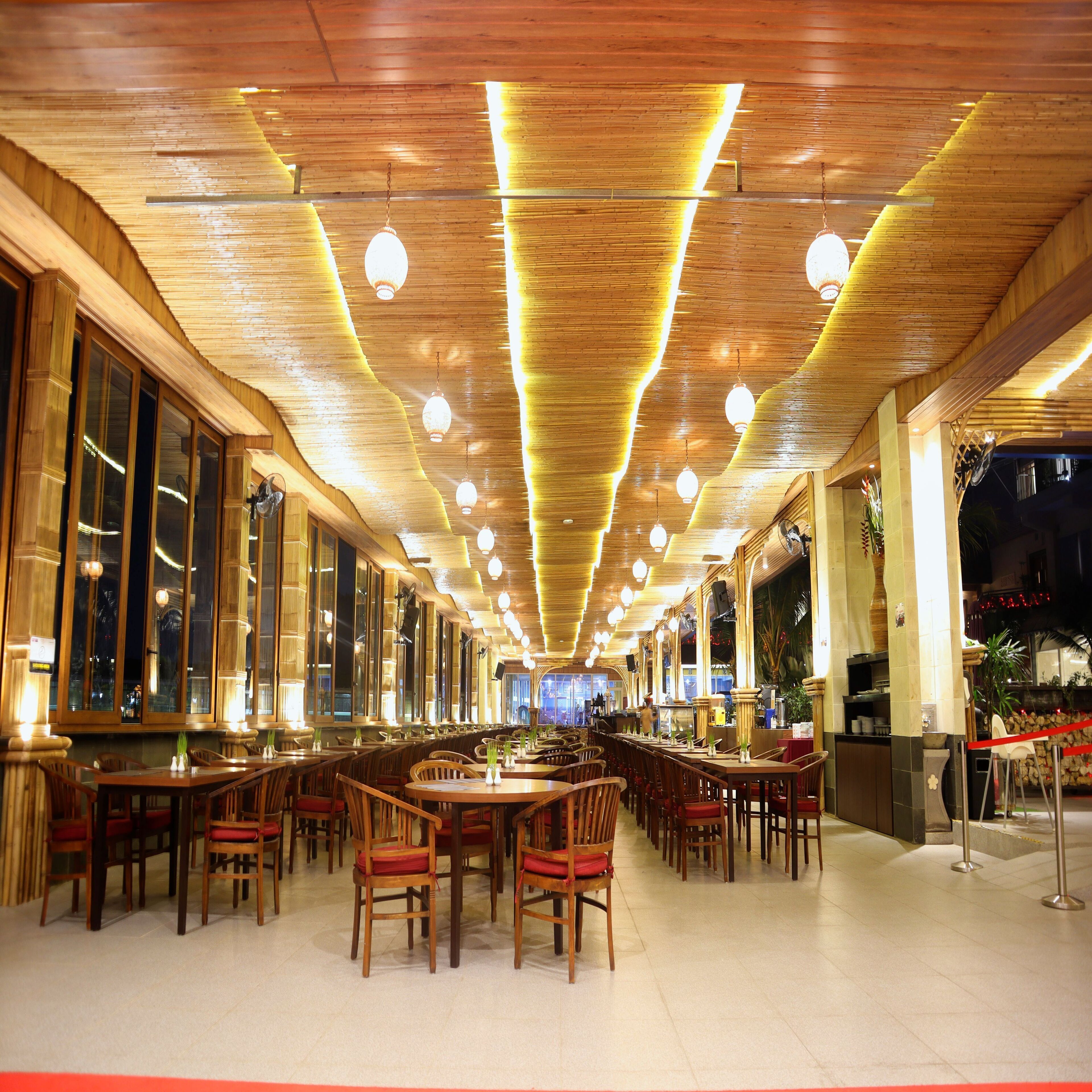 Un restaurante espacioso con vigas de techo de madera, lámparas colgantes y una barra larga con varias mesas y sillas.