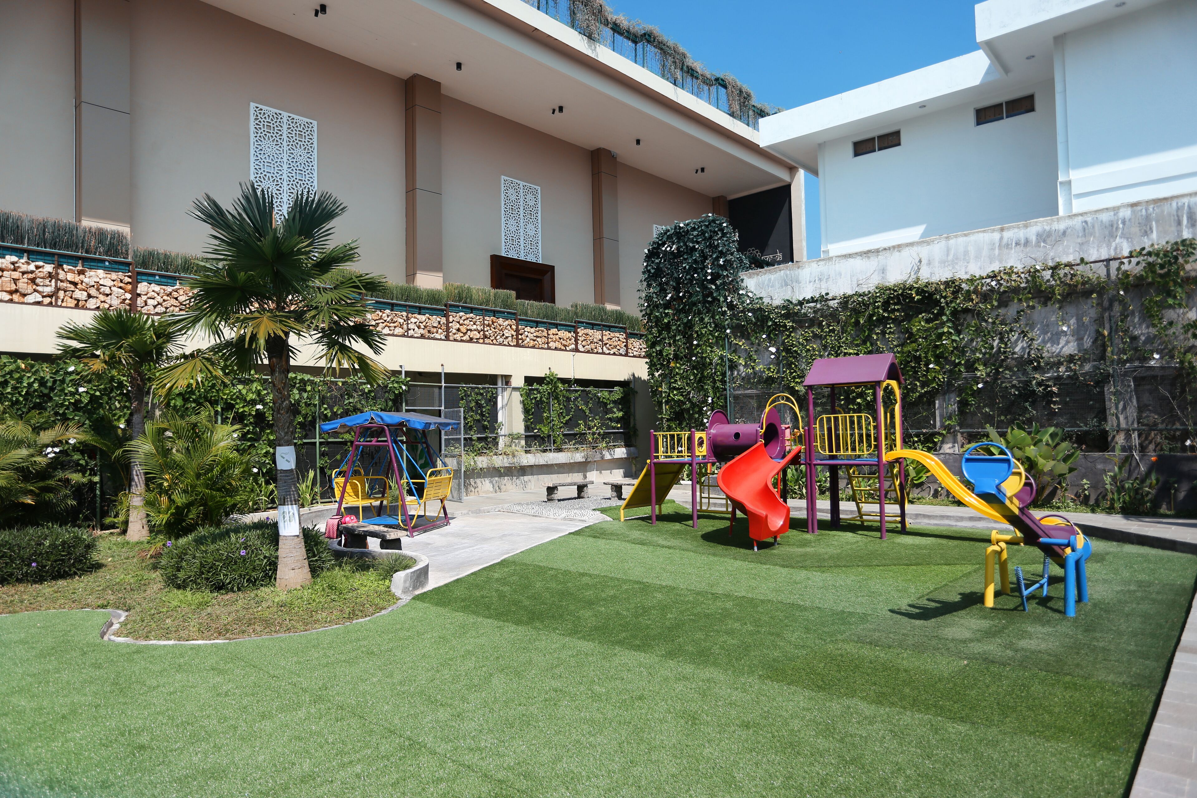 A playground with slides and climbing structures, surrounded by a well-maintained lawn and a building with a balcony.