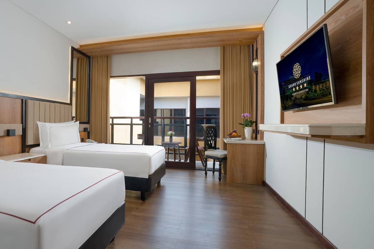 Une chambre d’hôtel avec deux lits, un bureau, une chaise et un téléviseur fixé au mur.