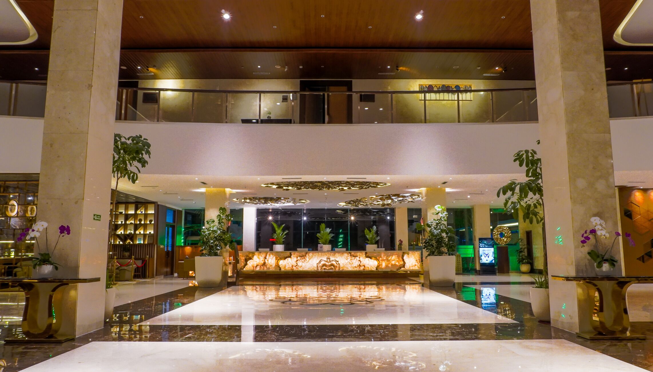A spacious lobby with a marble floor, a reception desk, and multiple potted plants.