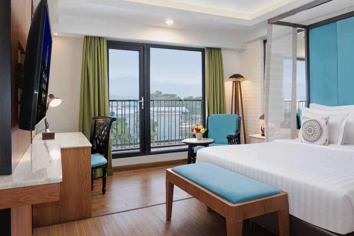 Une chambre d’hôtel avec un grand lit, un bureau, une chaise et une vue sur l’extérieur grâce à un balcon.