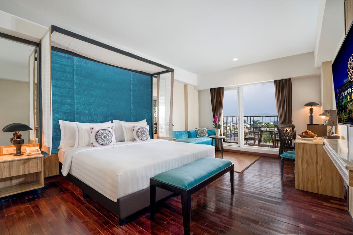 Une chambre d’hôtel spacieuse, dotée d’un grand lit, d’un balcon avec vue et d’un coin salon séparé.