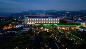 Un hotel de varios pisos, con un cartel llamativo que dice "Grand Sunshine Resort & Convention" y un estacionamiento con coches.