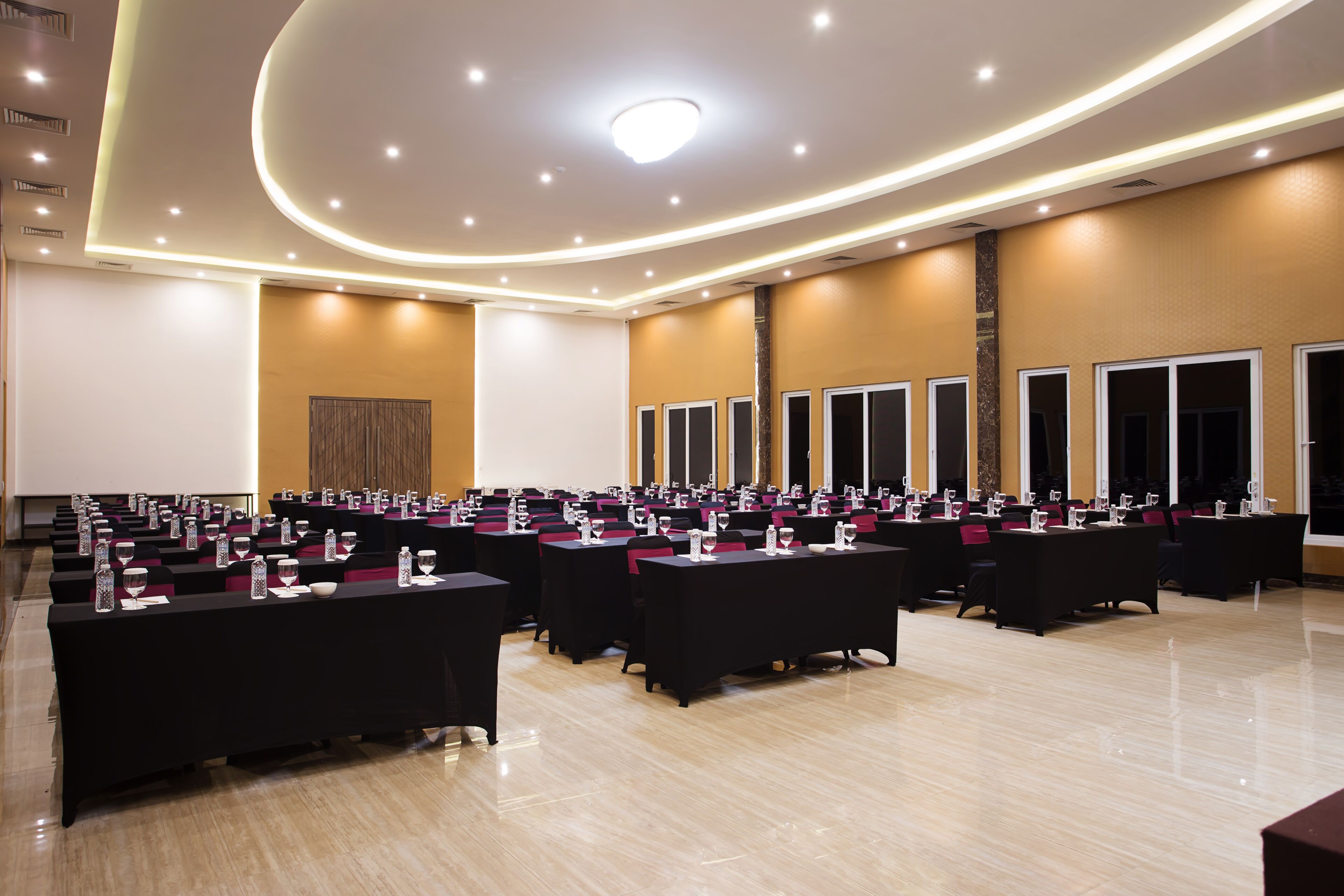 Une salle de conférence dotée de plusieurs tables, chacune équipée de verres d’eau et de blocs-notes, disposées en rangées.
