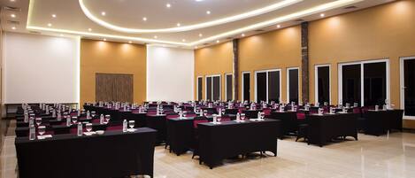 A conference room with multiple tables, each equipped with water glasses and notepads, arranged in rows.