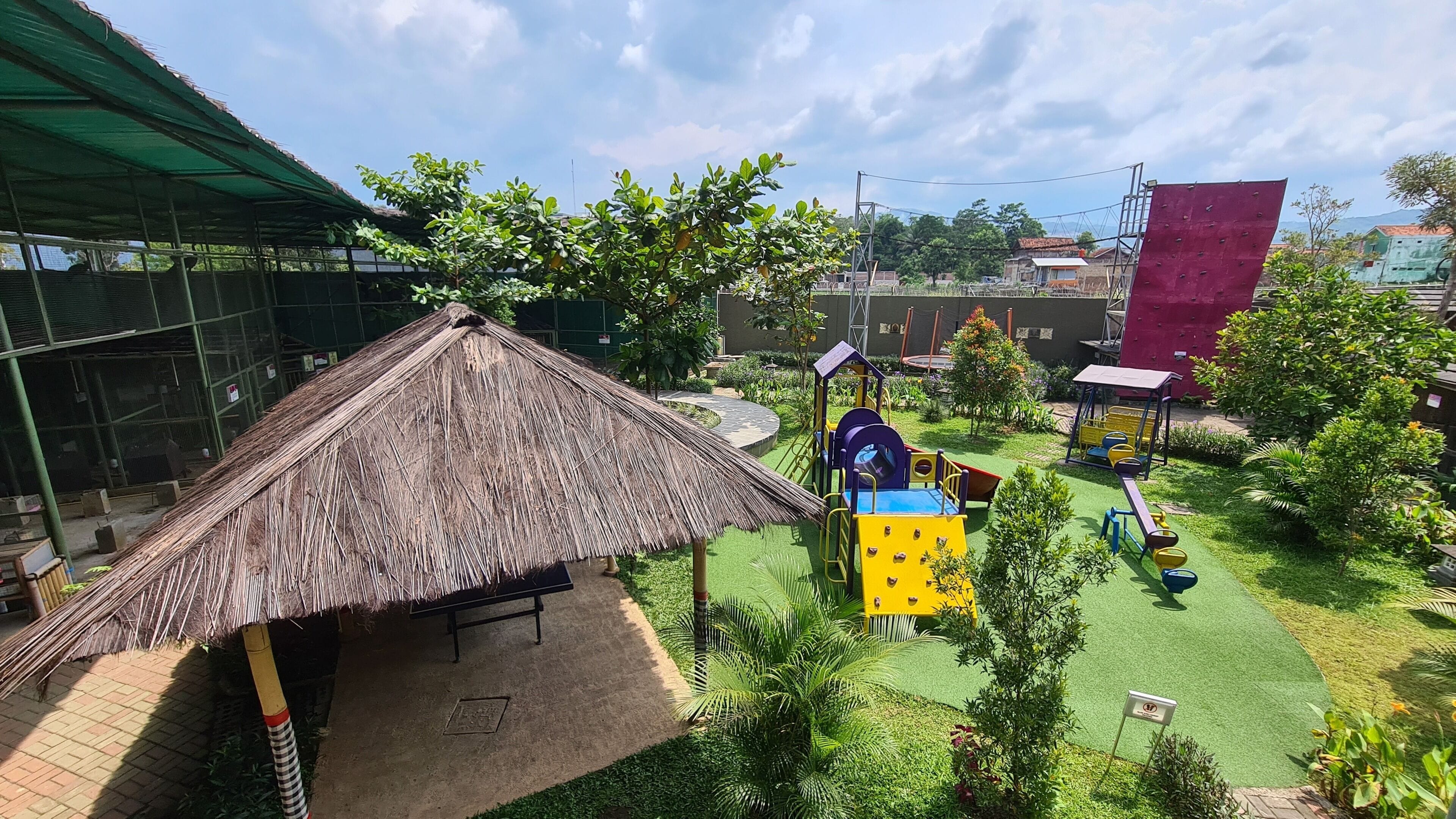 A playground with a thatched-roof structure, green artificial turf, and various play equipment.