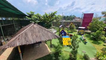 A playground with a thatched-roof structure, green artificial turf, and various play equipment.
