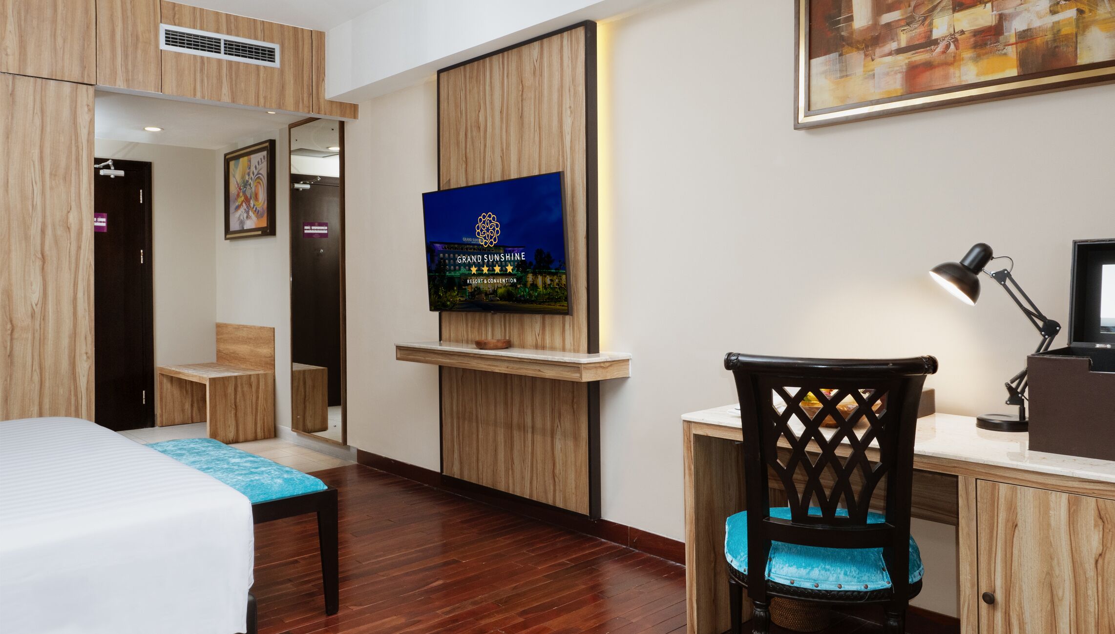 A hotel room with a bed, a desk with a chair, a television, and a painting on the wall.