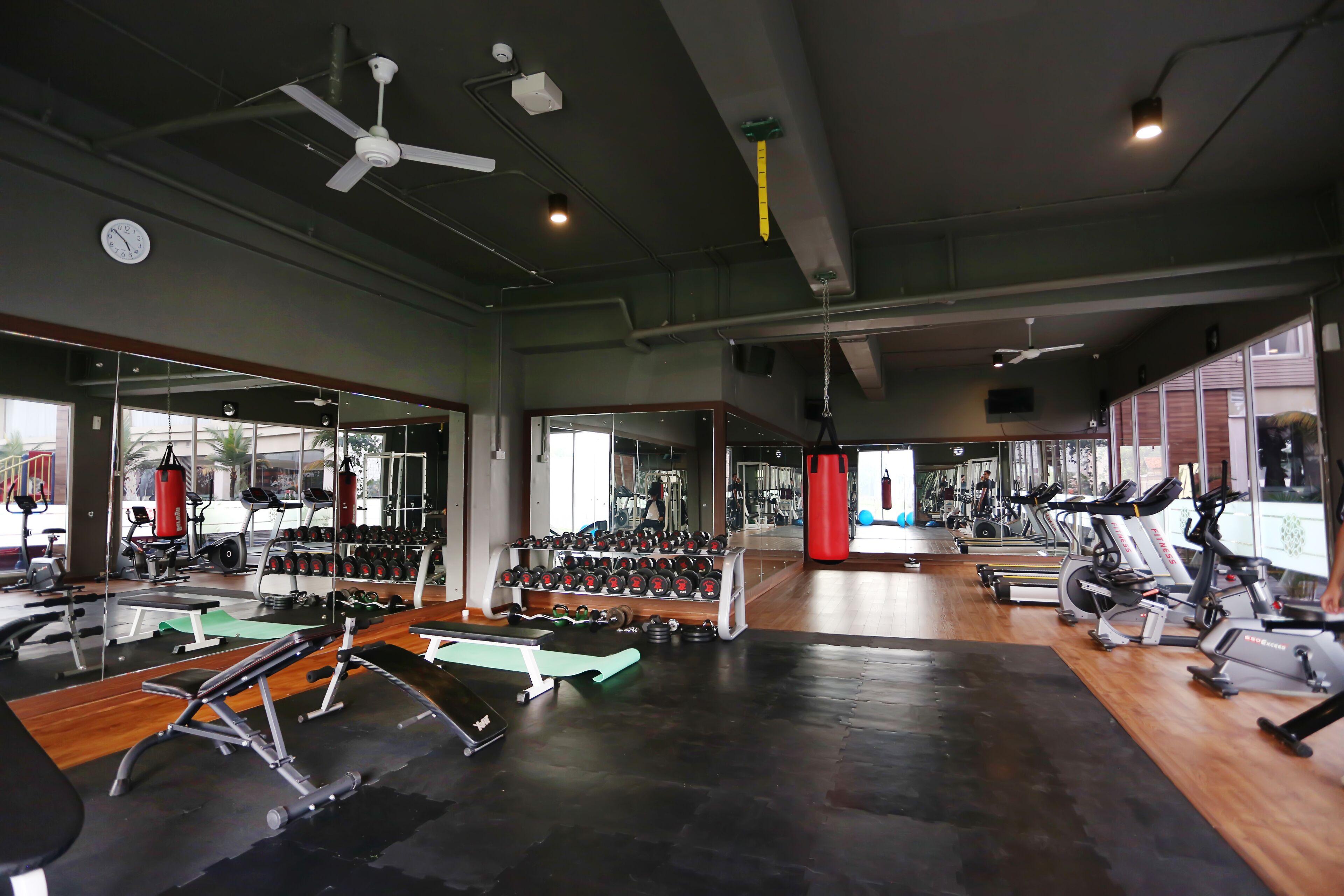 A gym with various exercise equipment, mirrors, and a wooden floor.