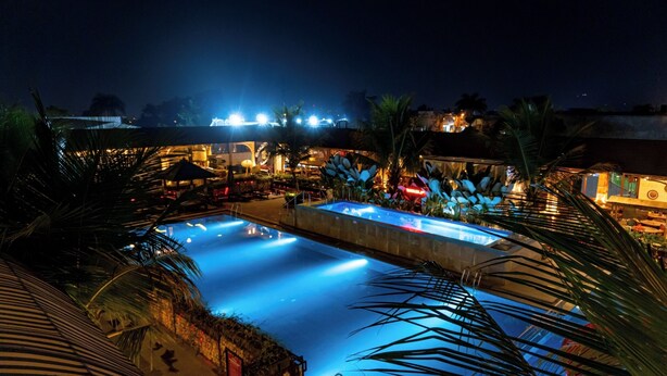 A nighttime view of a resort with a large swimming pool, palm trees, and illuminated buildings. - Grand Sunshine Resort & Convention (Soreang)