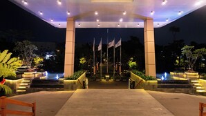A nighttime entrance with a covered walkway, flagpoles, and illuminated steps leading to a pool area. - Grand Sunshine Resort & Convention (Soreang)