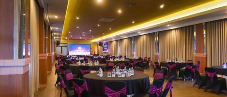 A conference room with round tables, chairs with pink sashes, and a large screen at the front.