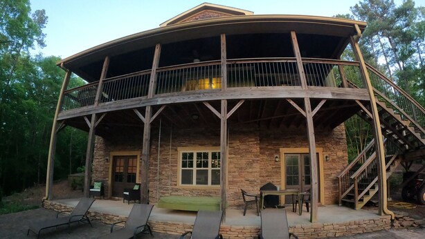 A rustic cabin with a stone exterior, a balcony with wooden railings, and a patio area with lounge chairs. - Lake Wedowee Privacy (Wedowee)