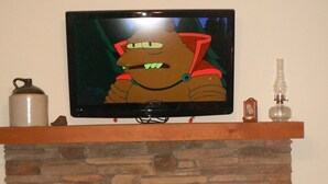 A television mounted above a stone fireplace with a television remote and decorative items on the mantel. - Lake Wedowee Privacy (Wedowee)
