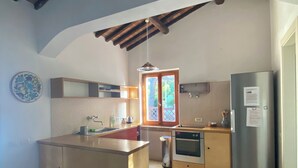 A kitchen with a central island, wooden cabinets, a stainless steel refrigerator, and a window with a view of greenery. - House With Sea View On Elba Island - 10 Min Walk from Beach (La Guardia)