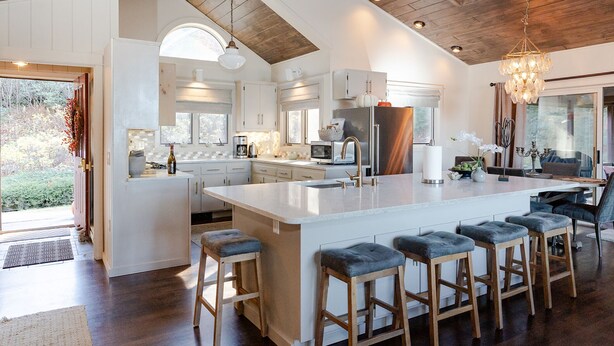 Een ruime keuken met een groot eiland, houten barstoelen en een kroonluchter.