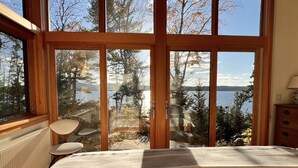 Un dormitorio con un ventanal grande que da a un lago y árboles.