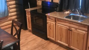 A compact kitchen with wooden cabinets, a built-in microwave, a stove, and a sink. - Cabin #8 (Garden City)
