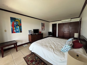 A bedroom with a bed, a desk, a chair, a TV, and artwork on the walls.
